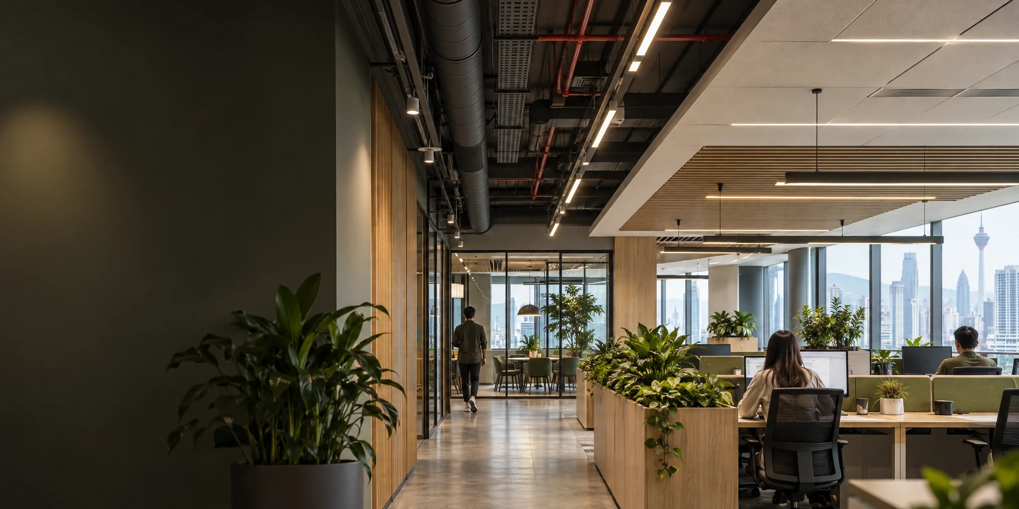 Neatly coordinated ductwork, pipes and cable trays in an exposed ceiling beside a finished office ceiling with linear lights